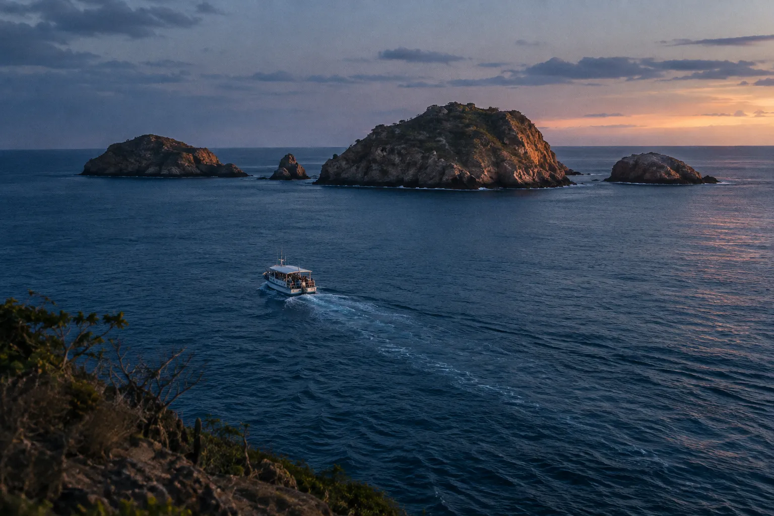 A tour boat crosses the ocean toward rocky islands at sunset.