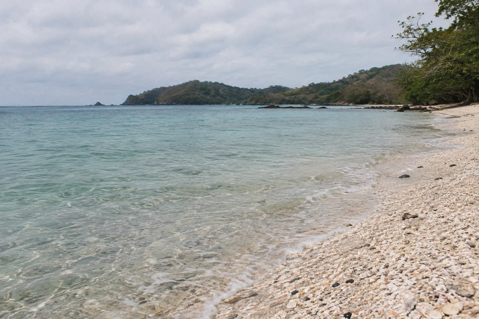 A quiet Costa Rican beach with clear shallow water and wooded hills across the bay.