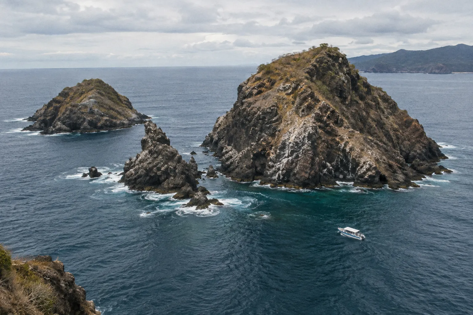 Rocky offshore islands rise from the ocean near a small boat.