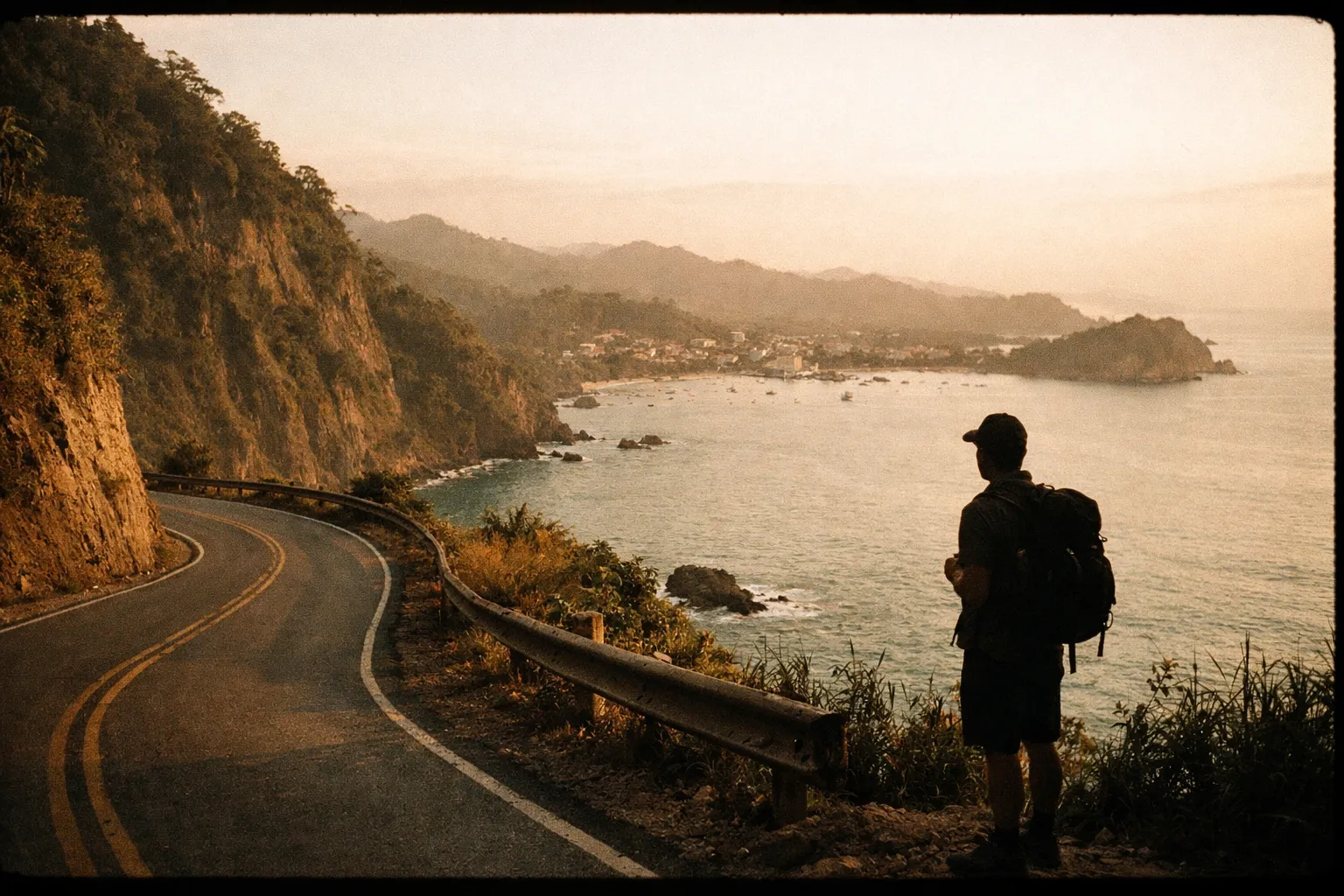 Lone silhouette of a traveler with a backpack standing on a cliff edge above a winding coastal road approaching Quepos, with lush rainforest and the Pacific Ocean below at golden hour