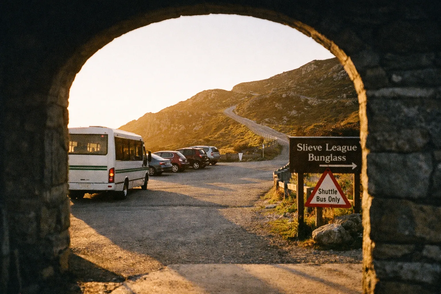 A shuttle bus and parked cars at the Slieve League Bunglass entrance with hills in the background.