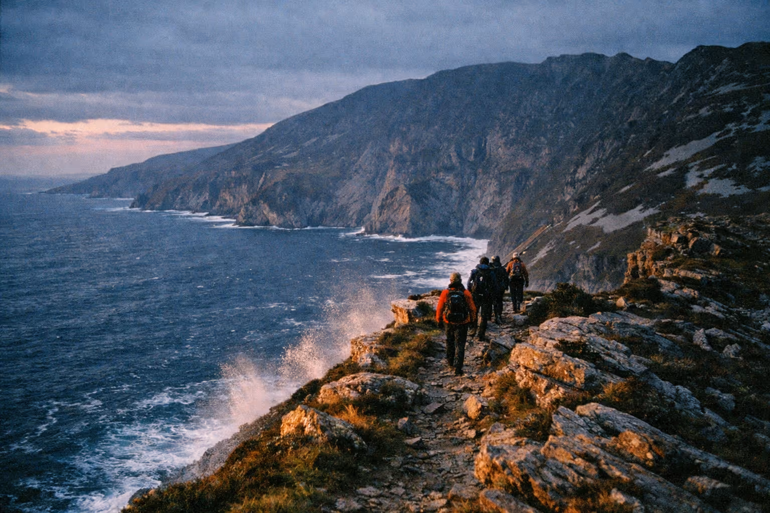 Hikers walk along a rocky path beside the sea cliffs at Slieve League in Ireland.