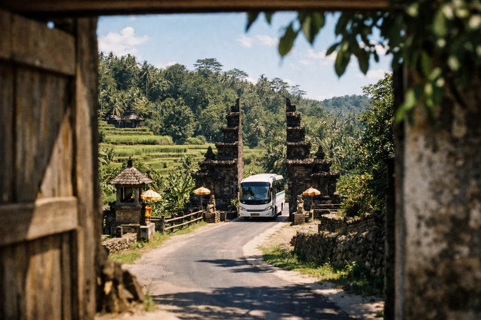 A bus drives through a traditional Balinese gate near the Tegallalang rice terraces in a lush green landscape.