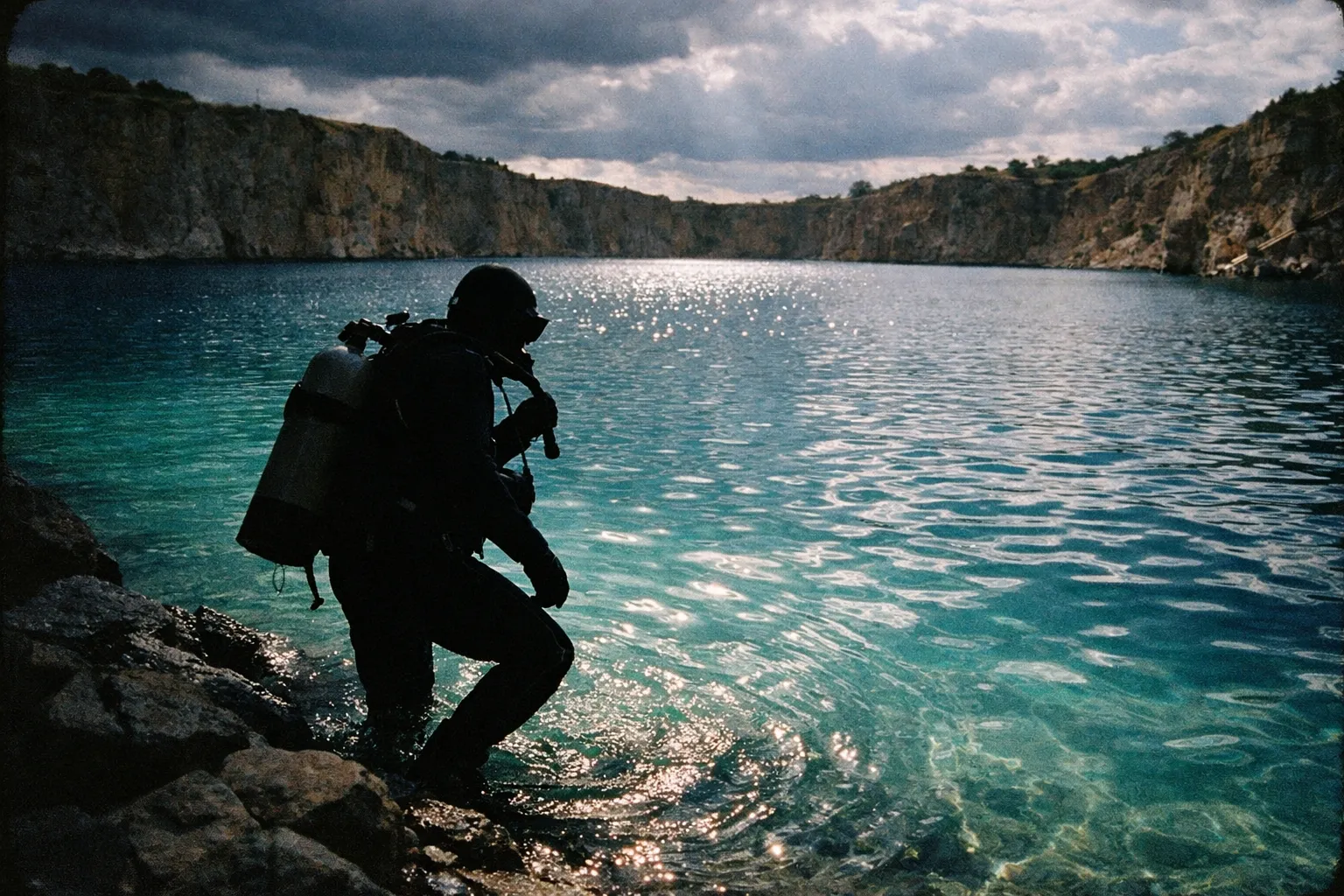 Silhouette of a diver entering turquoise water at the quarry edge with rocky backdrop