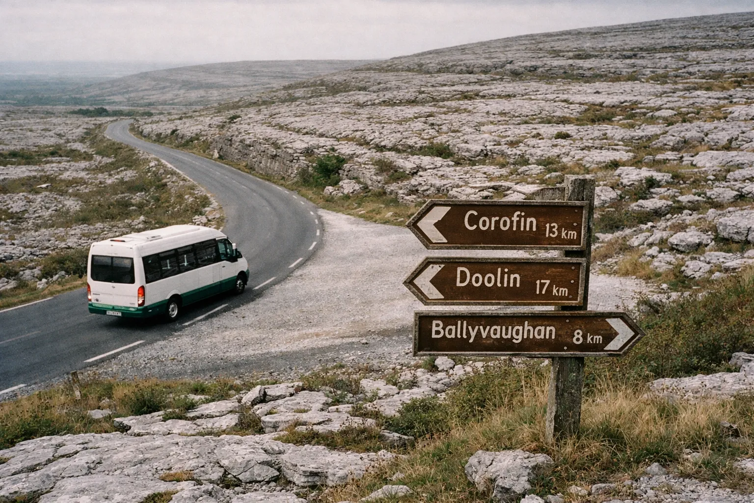 A minibus drives along a winding road in the rocky landscape of the Burren near a signpost to local towns.