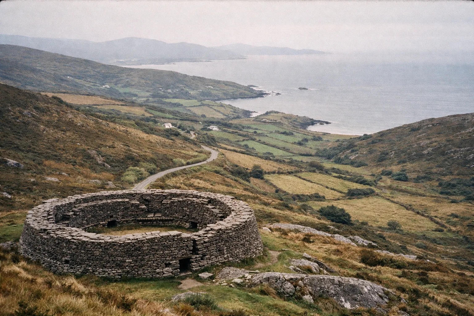 Stone fort stands on a hillside overlooking fields and coastline along the Ring of Kerry in Ireland.