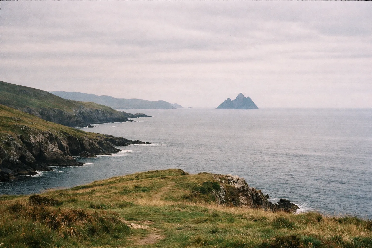 The Skellig Islands seen from a grassy cliff along the rugged Ring of Kerry coastline in Ireland.