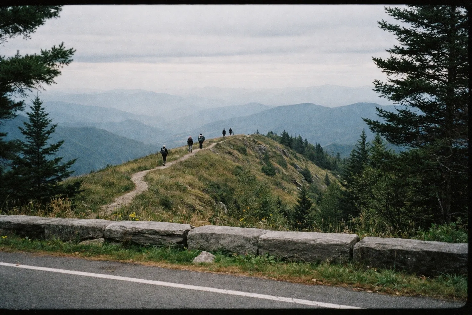 Hikers walk along a mountain ridge trail surrounded by forested hills in the Great Smoky Mountains.