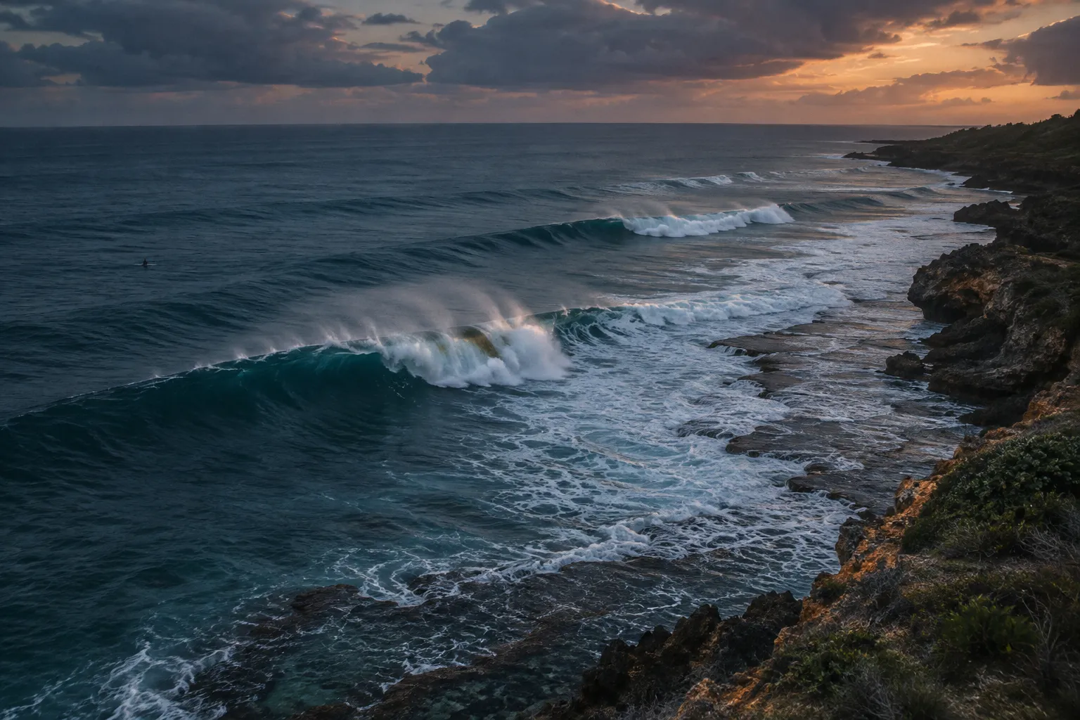 Waves break along a rocky coastline at sunset.
