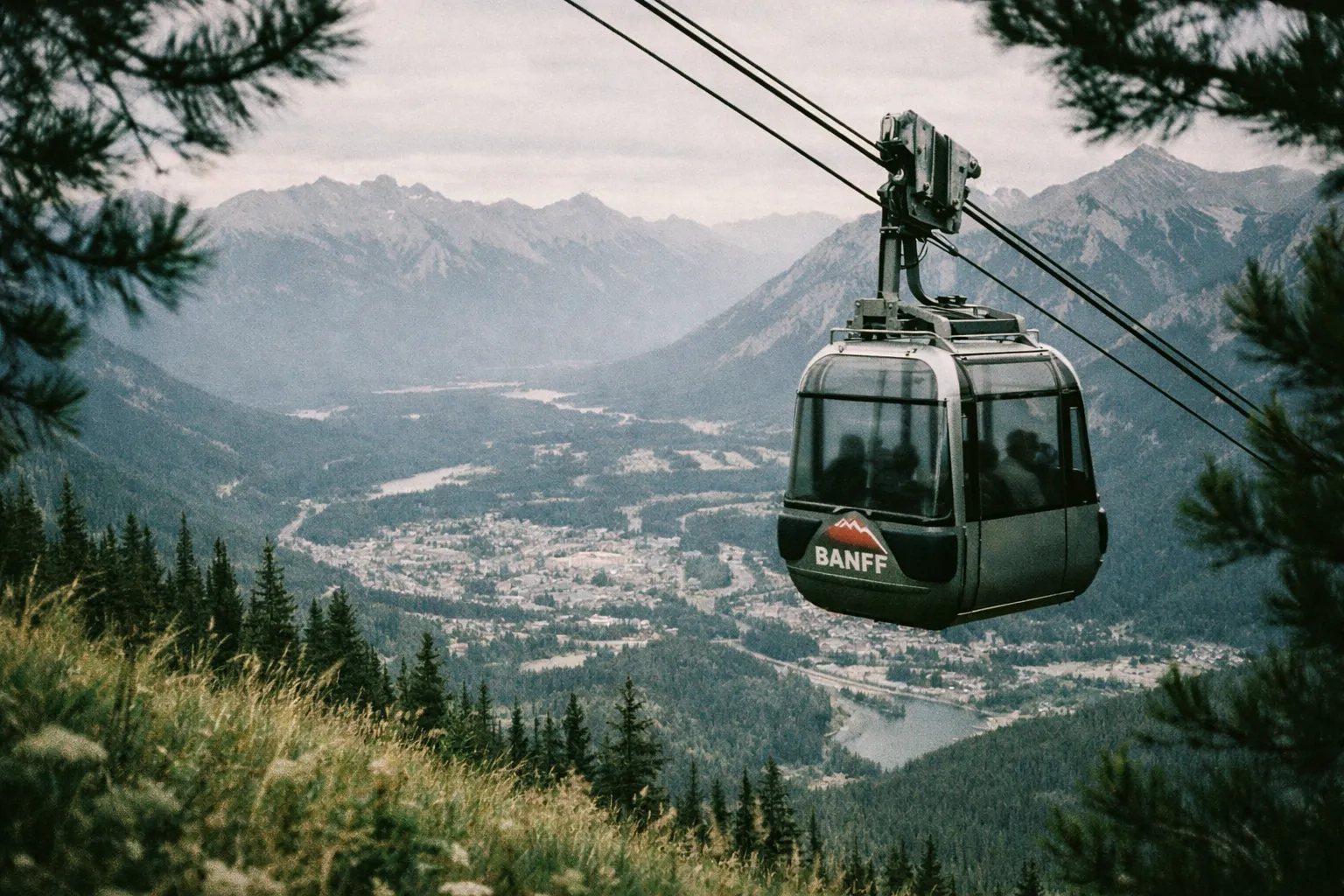 A Banff gondola travels above a forested slope with mountains and the town of Banff visible in the background.