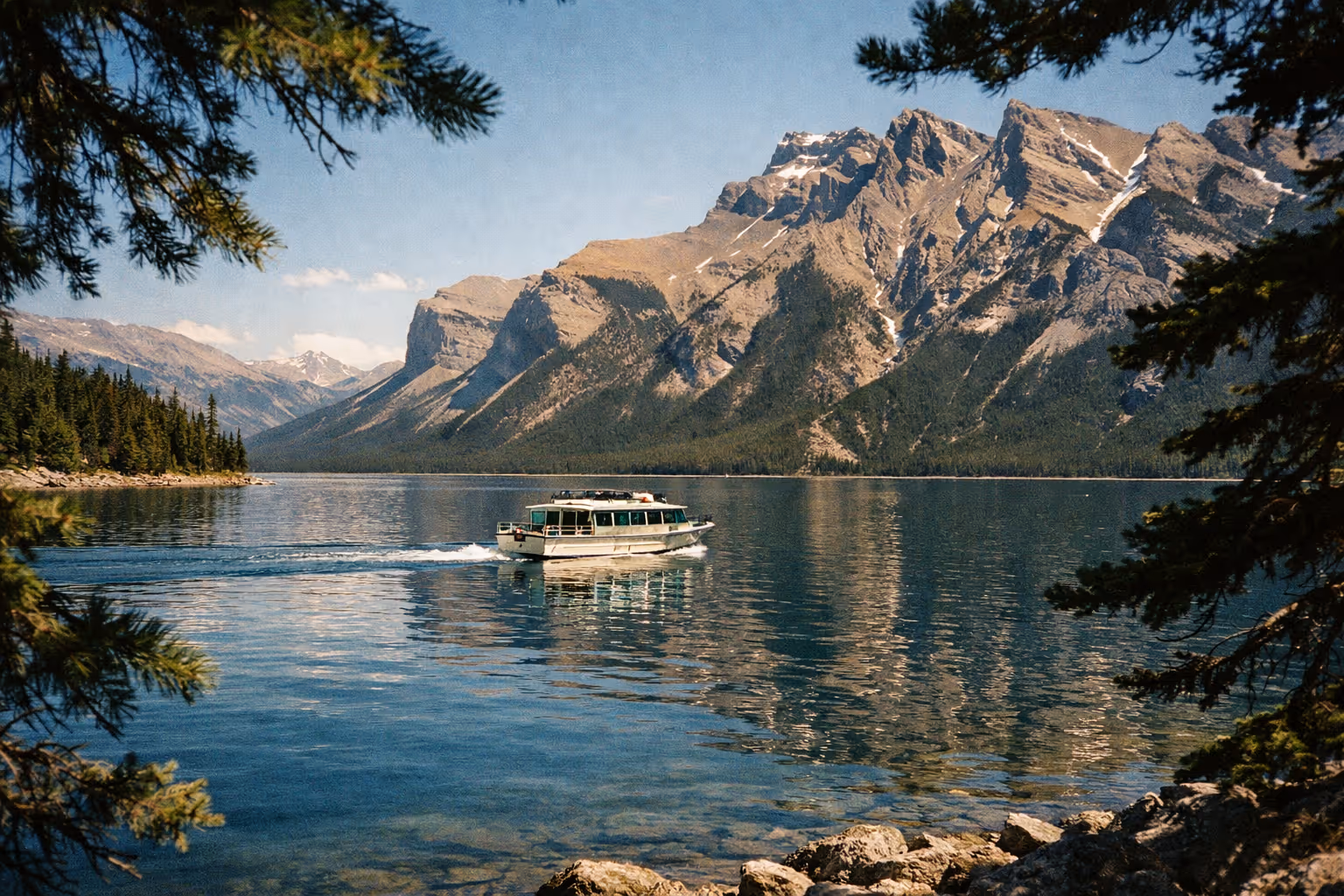 A tour boat cruises on Lake Minnewanka with mountains and pine forest in the background.