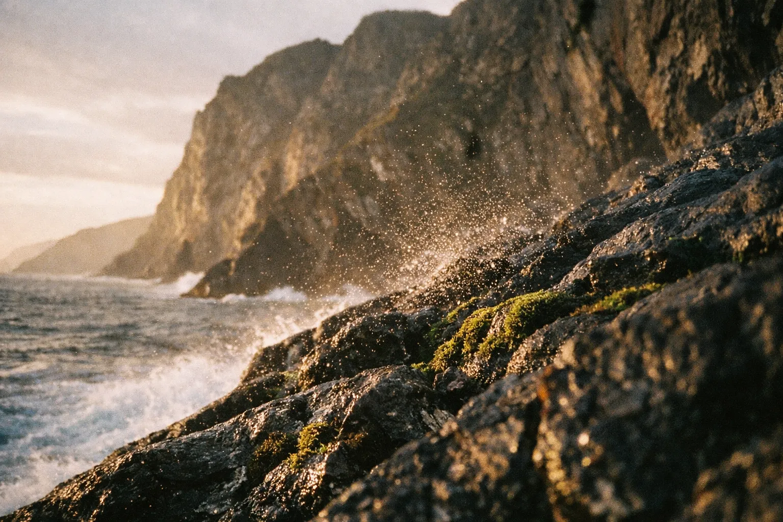 Waves crash against rocky cliffs along a rugged coastline at sunset.