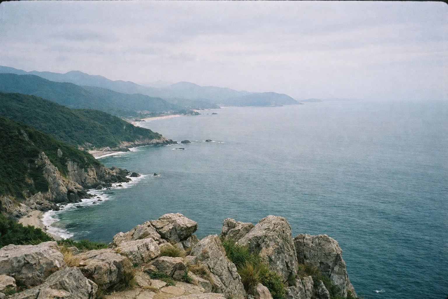 Rocky coastline with green hills and the sea viewed from a high vantage point.