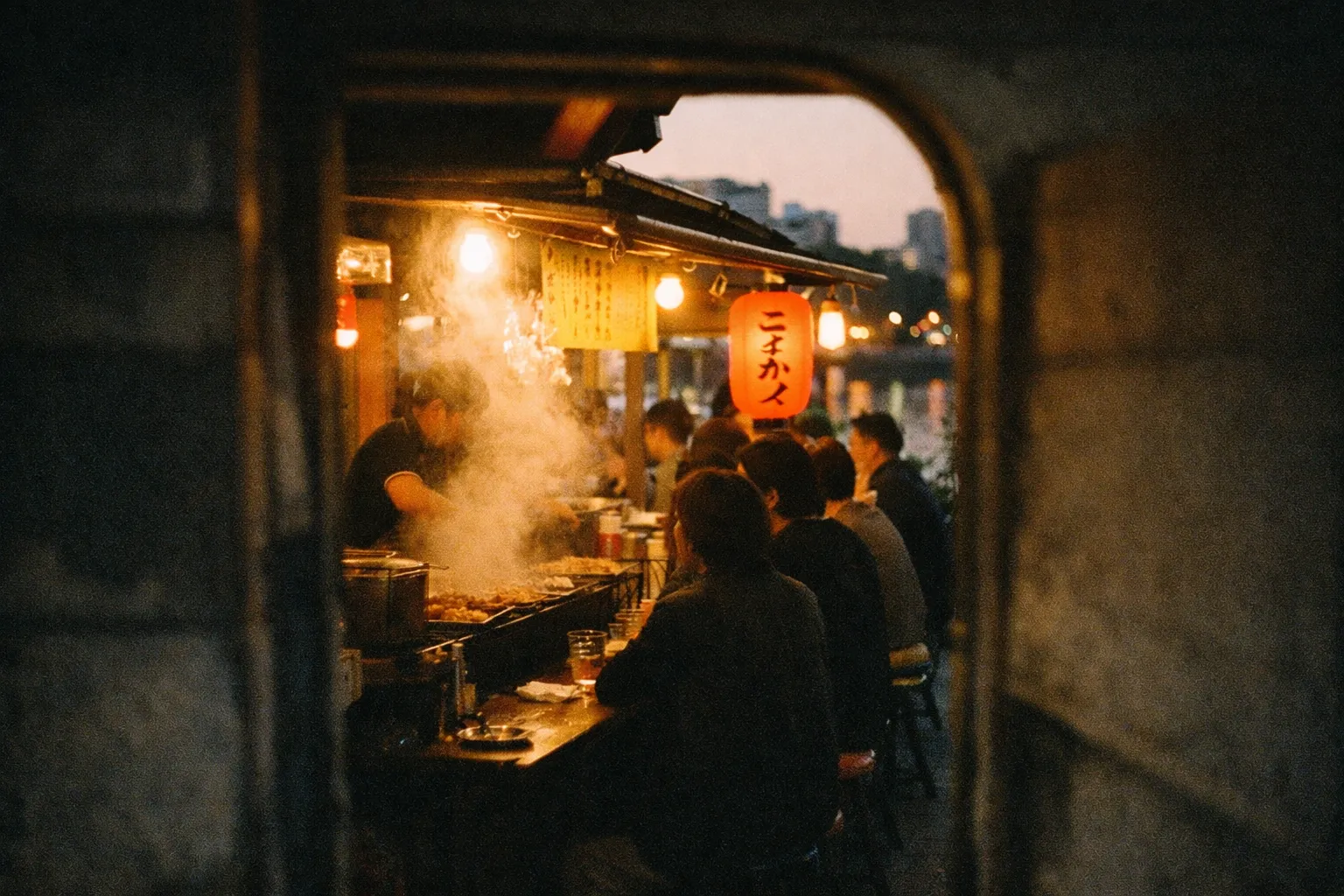 People dining at a yatai food stall along a riverside in Fukuoka at dusk.