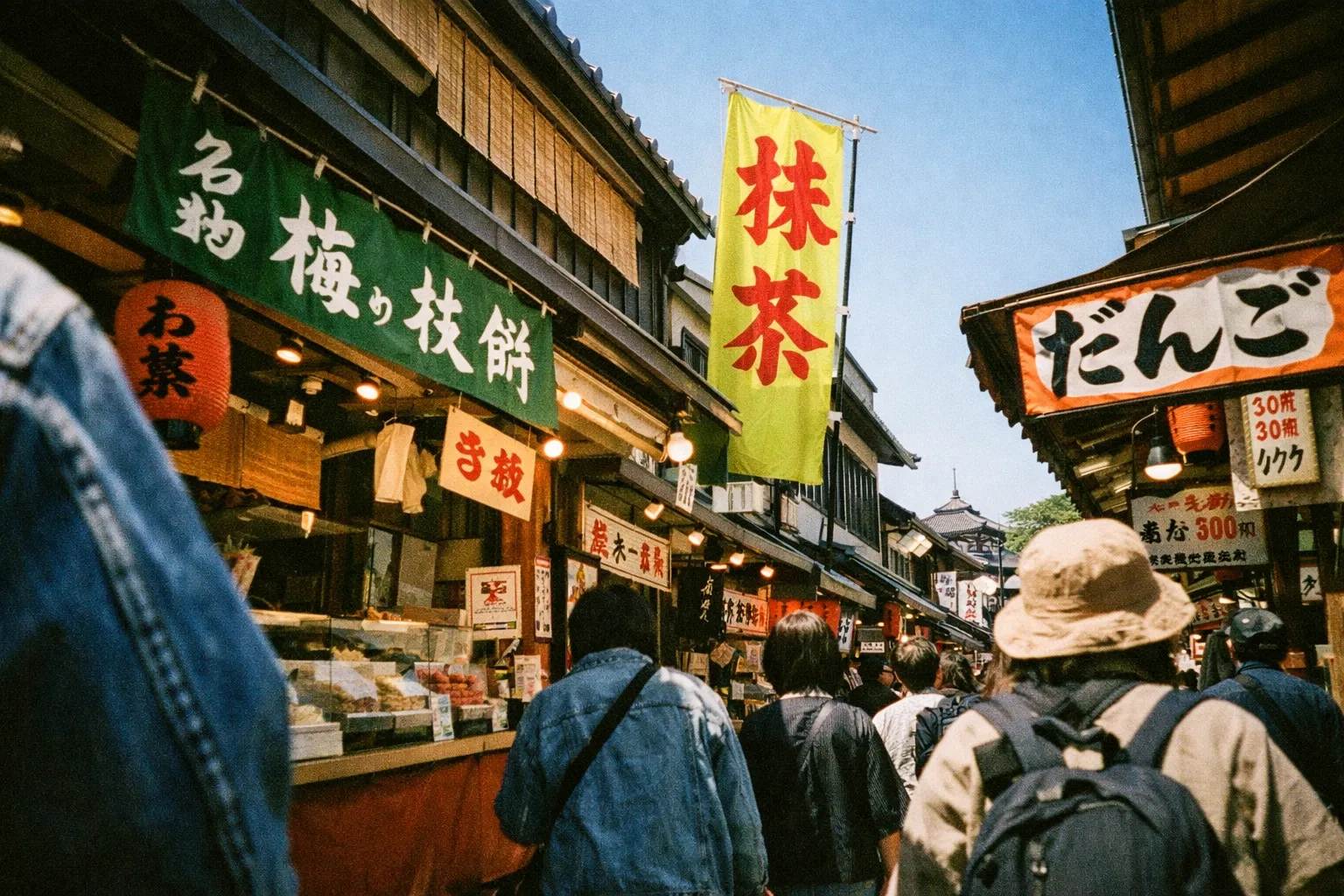 People walk along a busy street lined with food stalls and Japanese signs in a traditional market area.