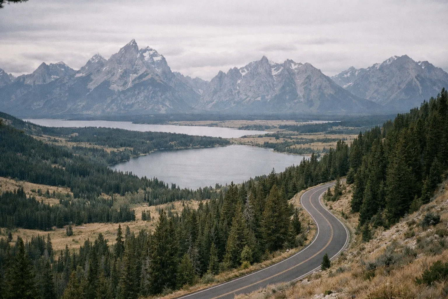 A winding road leads through forests toward Jenny Lake with the Teton mountains in the background.