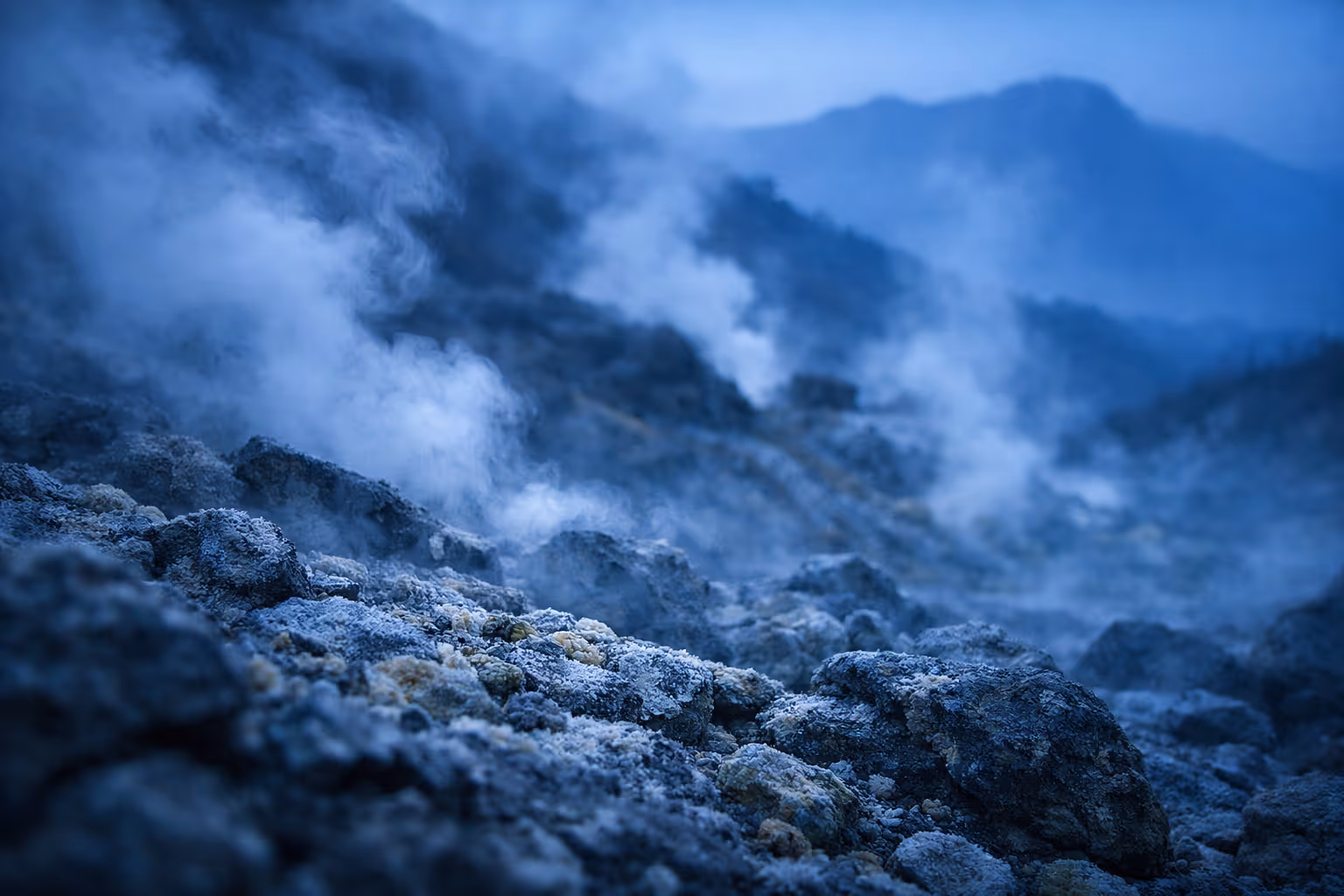 Steam rises from rocky terrain in the Owakudani volcanic valley with mountains in the background.