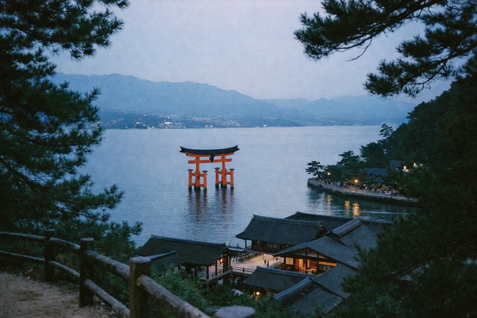 The iconic red torii gate of Itsukushima Shrine rises from the water off the coast of Miyajima Island at dusk.