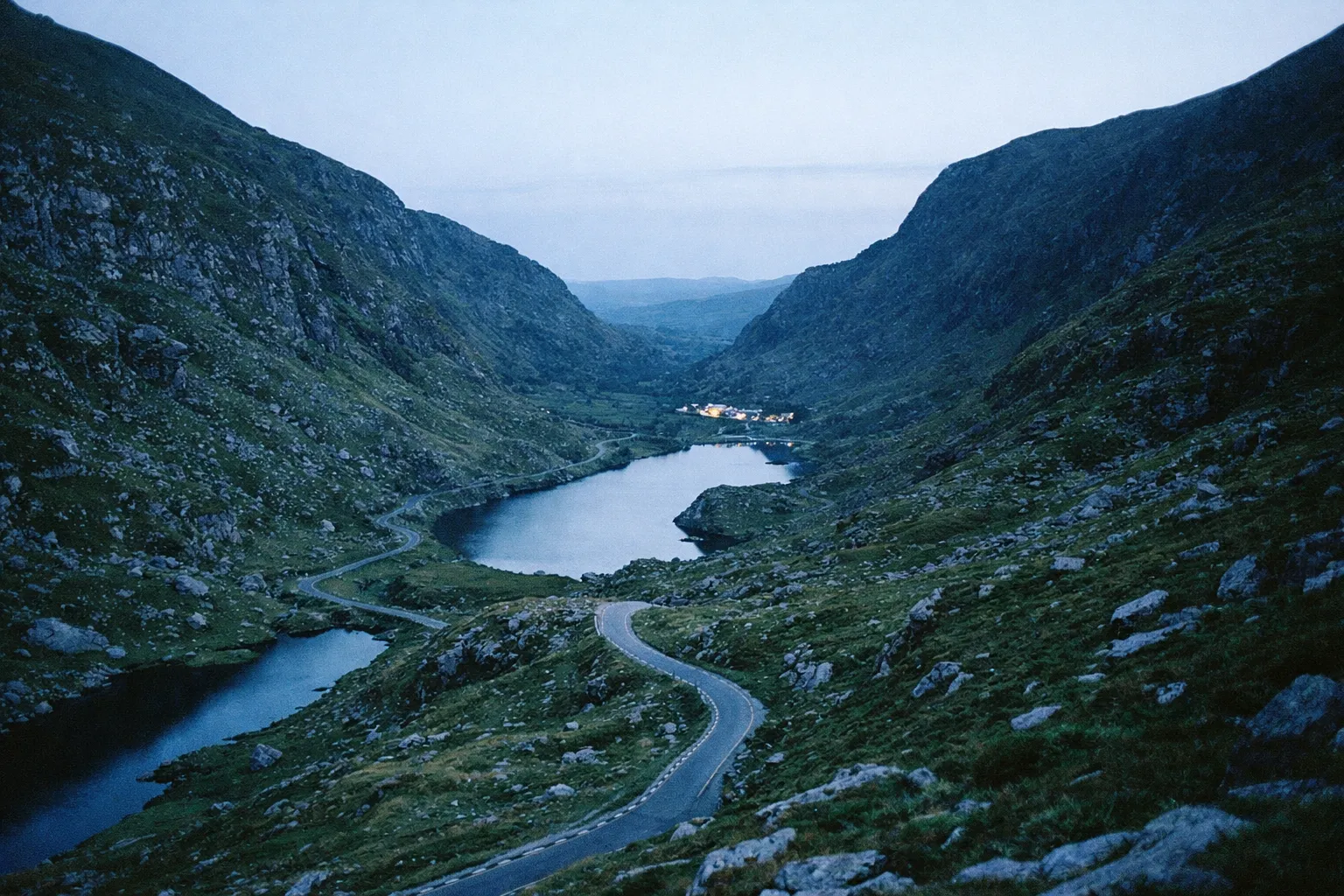 Winding road passes lakes and steep mountains in the Gap of Dunloe at dusk.