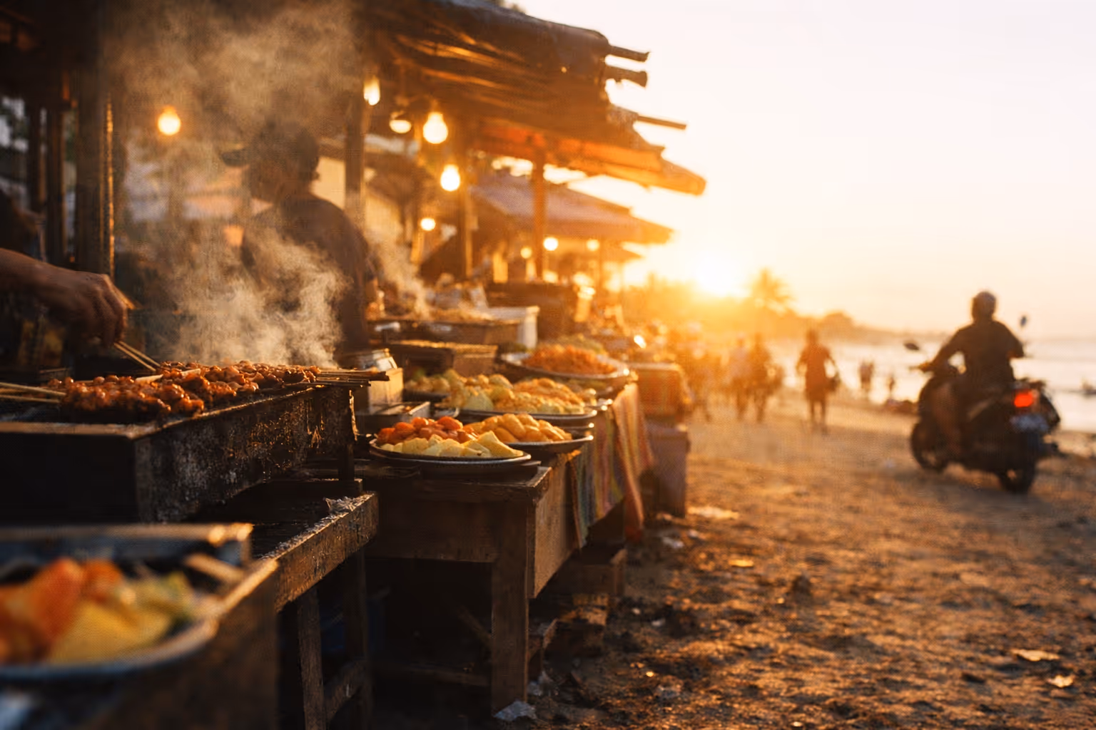 Street food stalls grilling skewers and serving dishes along a busy beach at sunset in Kuta, Bali.