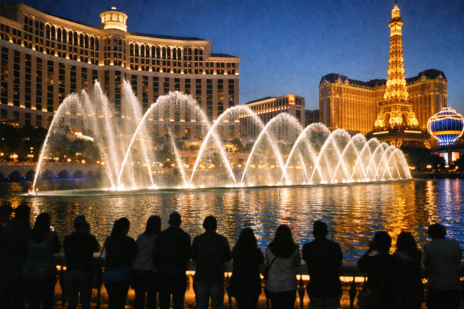 People watch the Bellagio fountain show with the Paris Las Vegas hotel in the background on the Las Vegas Strip at night.