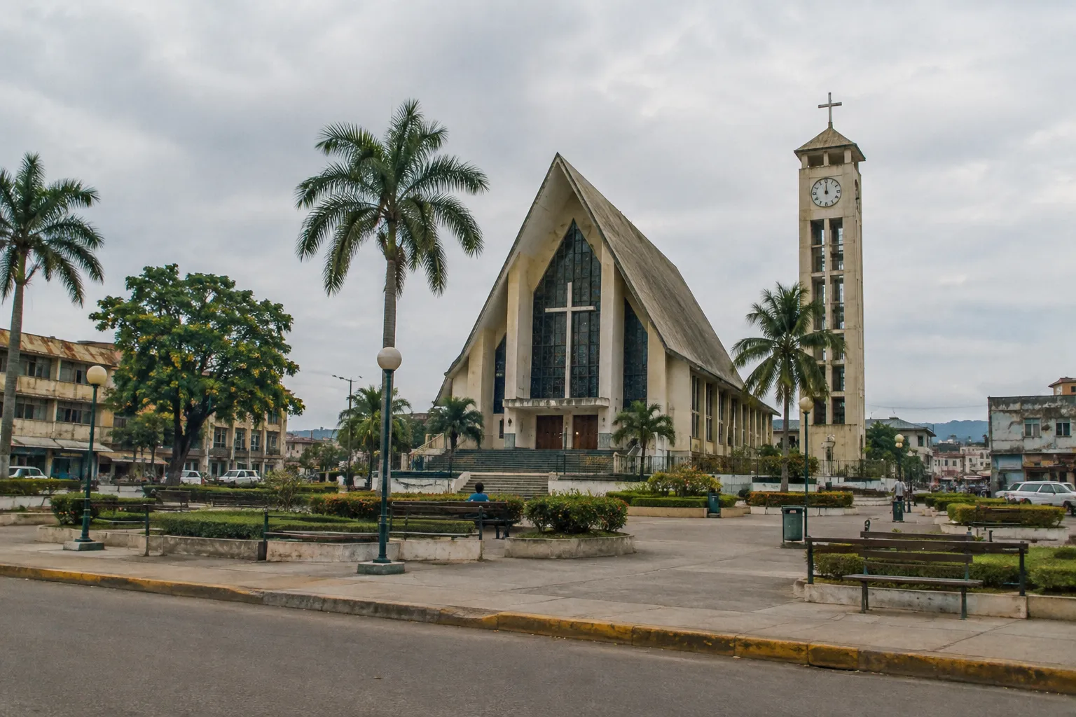 A modern church and clock tower stand in a palm-lined town square.