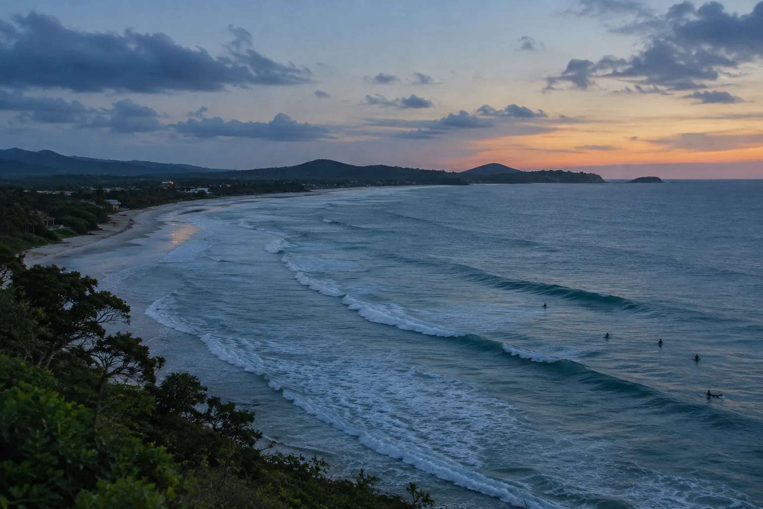 Surfers ride waves along a Pacific beach in Costa Rica at sunset.