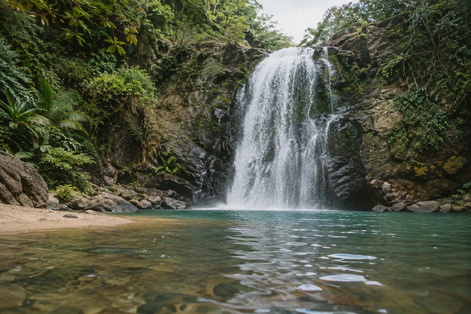 A waterfall plunges into a clear pool surrounded by dense tropical forest.