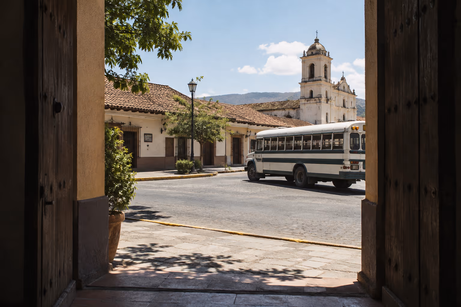 A bus passes a white church in Liberia, Costa Rica, viewed through an open doorway.