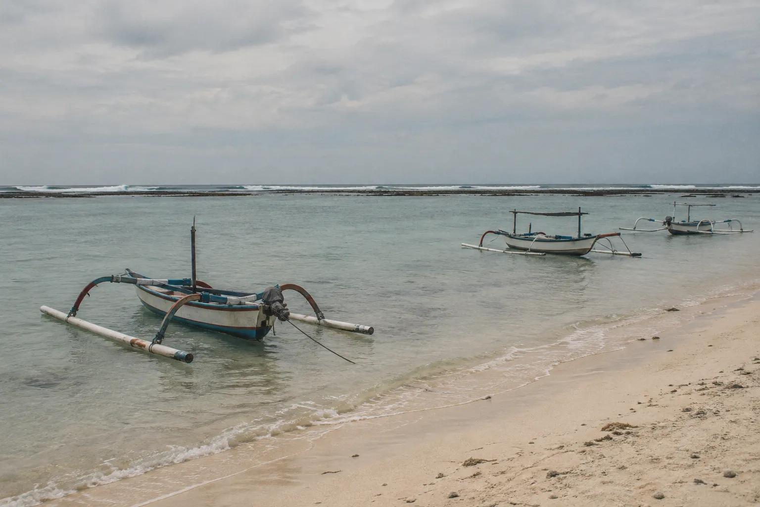 Traditional outrigger boats float in the calm shallows off Sanur Beach, Bali.