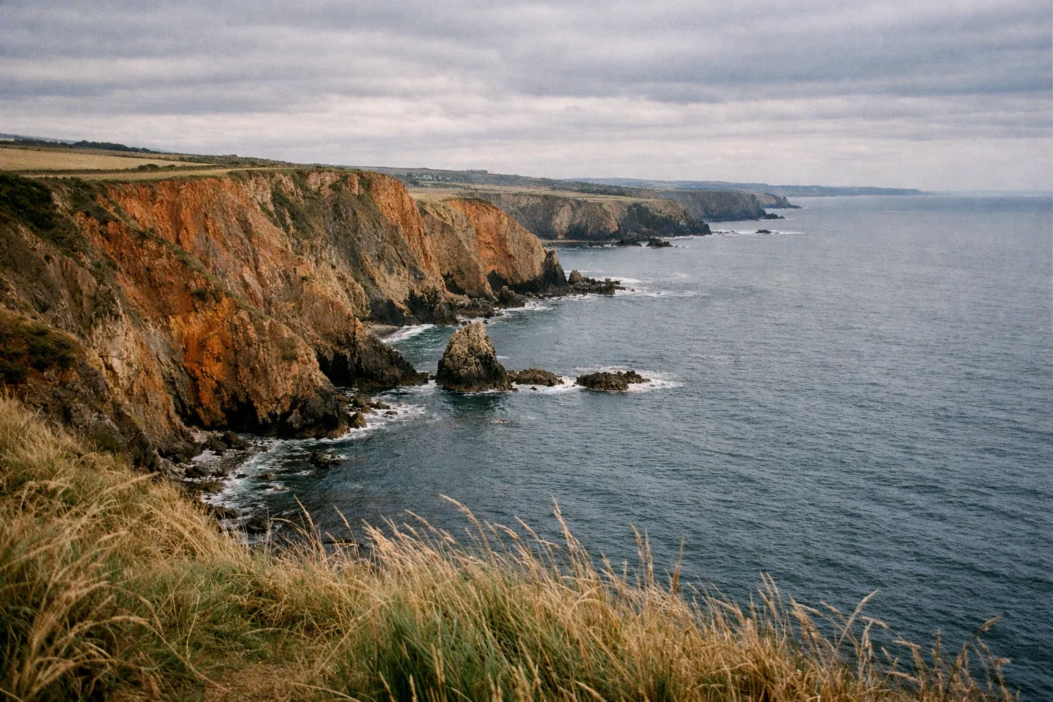 Cliffs along the coastline with grassy foreground and waves crashing against rocks below in Waterford, Ireland.