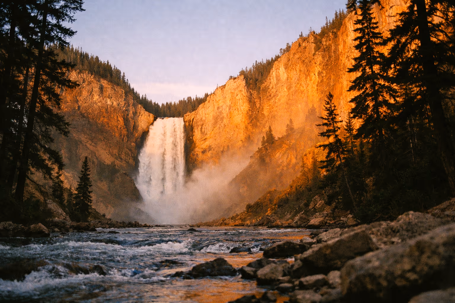 Lower Falls in Yellowstone National Park framed by cliffs and pine trees above a flowing river.