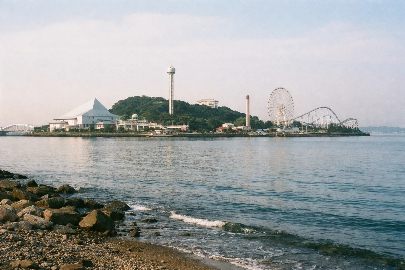 Yokohama's Sea Paradise amusement park seen across the water from a rocky shoreline.