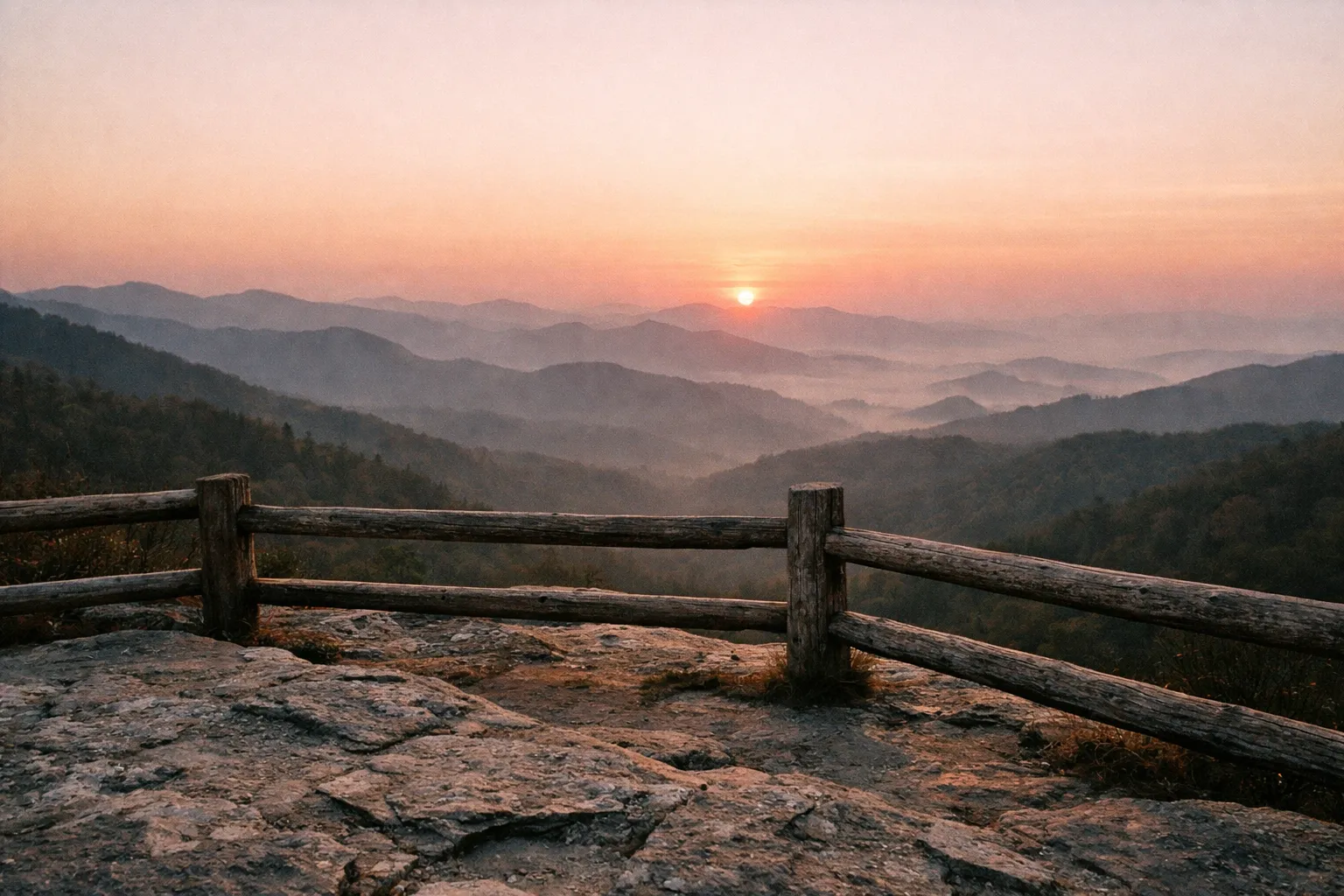 Golden sunrise over layered Smoky Mountain ridges, view from an overlook with a wooden railing