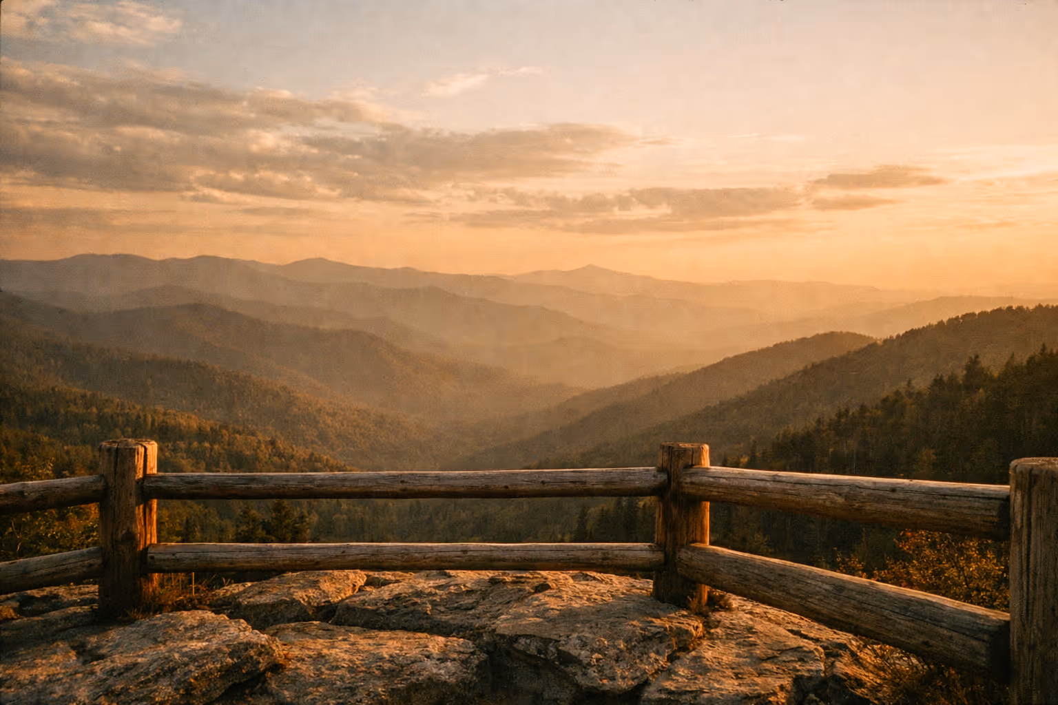 Golden-hour panorama of the Great Smoky Mountains seen from a scenic overlook with a wooden railing in the foreground