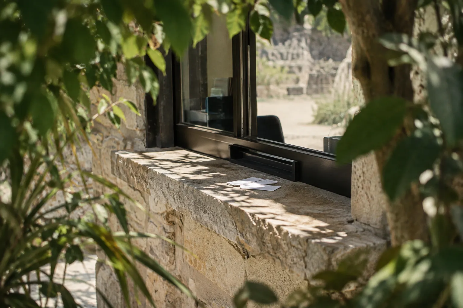 A stone ticket window sits among leafy trees at an archaeological site.