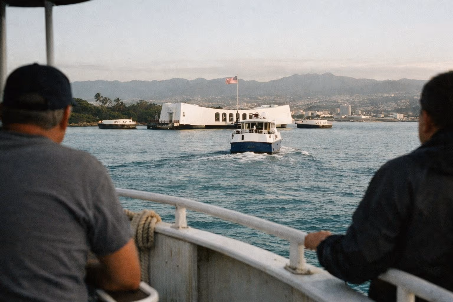 Visitors on a boat approach the USS Arizona Memorial at Pearl Harbor, with mountains in the background.
